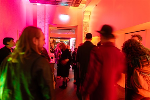 A group of people mingle in a hallway with orange and pink lights shining.