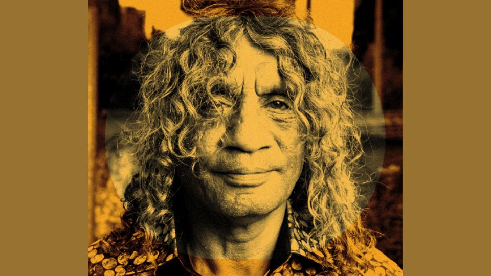 A man with curly long hair is wearing a collard shirt. He looks solemnly into the camera. A yellow hue is overlayed across the image.
