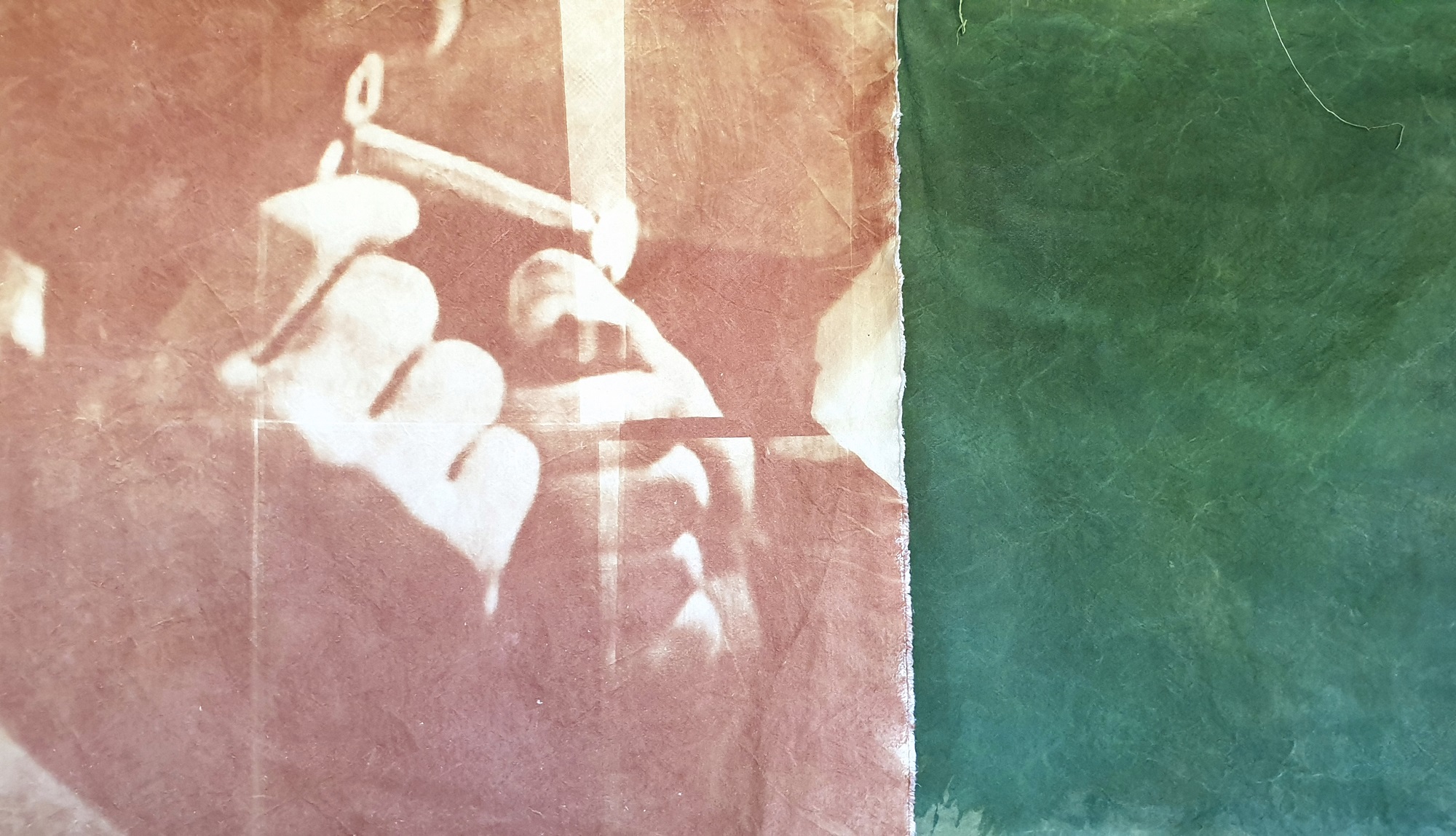 A brown and green UV exposure dye print on canvas with two hands holding a lighter by Jeremy Eaton
