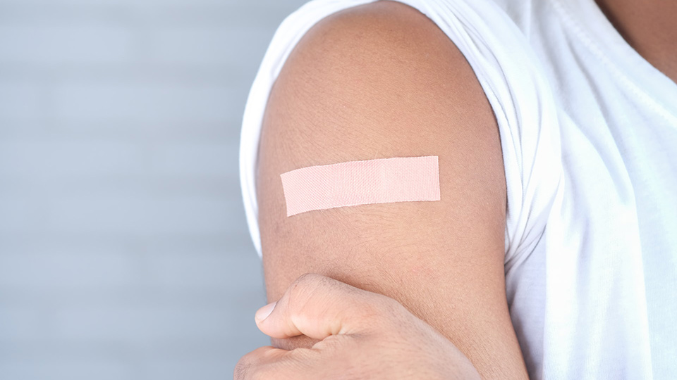 An adhesive bandage on a person's upper arm, suggesting a vaccination jab.