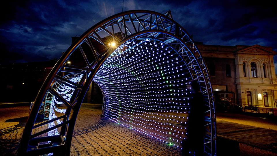 A tunnel shaped metallic cage with surrounding lights illuminating the night