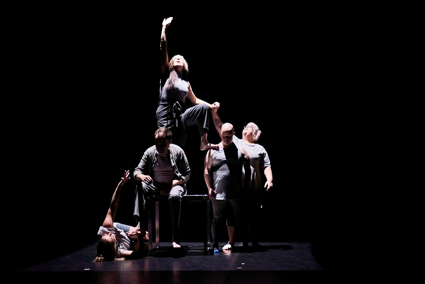 Several people creating a human pyramid on a theatre stage on a black background