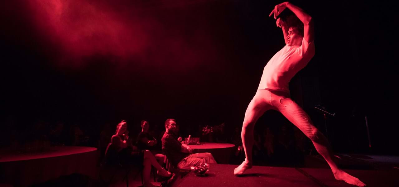 Dancer performs in front of a small group, in dim red light