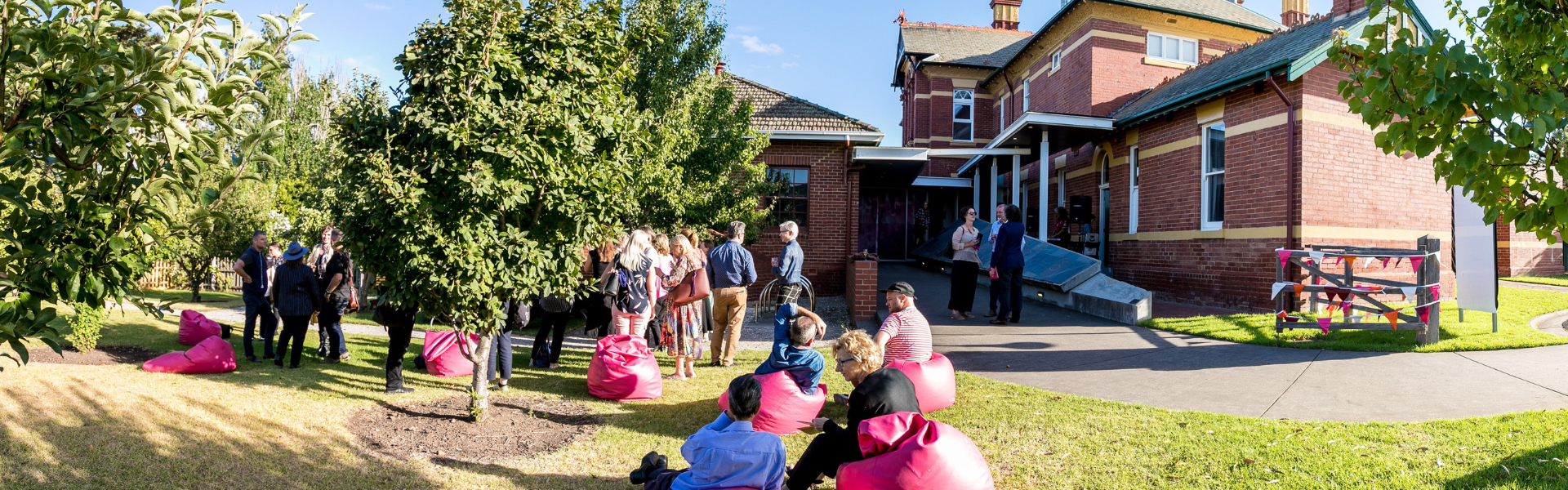 A group of people gather on the green grass outside Bundoora Homestead Art Centre