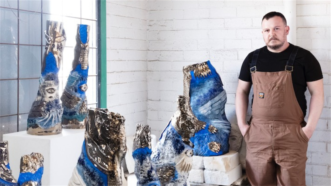 Artist Ara Dolatian stands in front of several blue ceramic scultptures