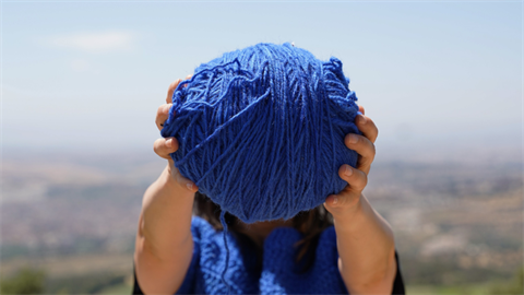 Two hands hold up a blue ball of wool