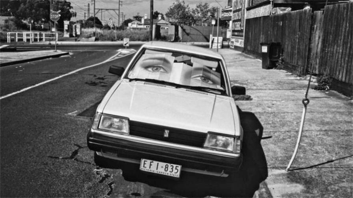 A parked car displaying a windscreen sun shade that displays two big eyes