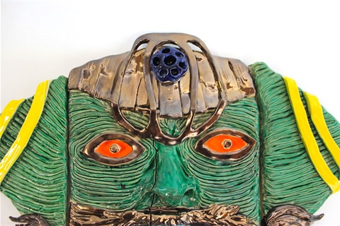 A green ceramic face with orange eyes and a gold head adornment 