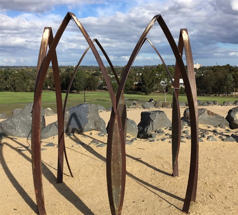 sculpture made from bands of steel formed into tall “crown-like or inverted “v” shapes”. The work has panels of etched copper with text in different languages riveted onto areas of the steel that overlap