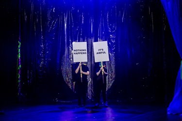 Two banners on sticks are held by people in a spotlight.