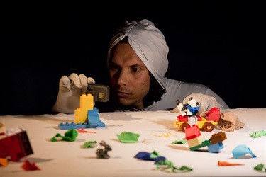 A person wearing a white hooded top crouches behind a table with Legos displayed over it.