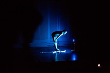 A person stands leaning over to look into a TV screen. A blue light glows on their face.