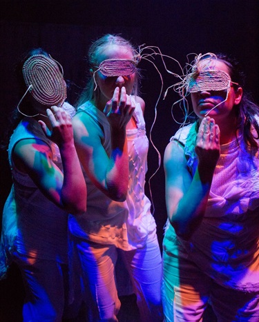 Three people wear abstract masks held up to their faces by the fingers.