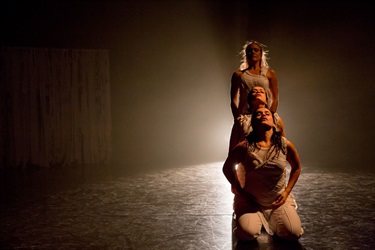 Three women stand behind one another to create a vertical cascade. A bright light shines from behind them.