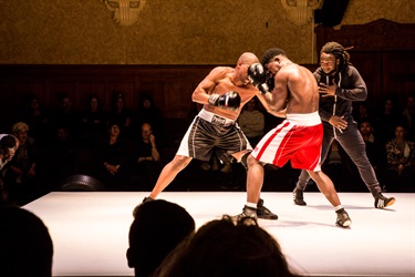 Two Black men box with a third Black man referring.
