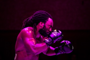 A Black man wearing boxing gloves glows in a pink hue.