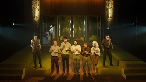 A group of people wearing costumes stand across a stage setting.