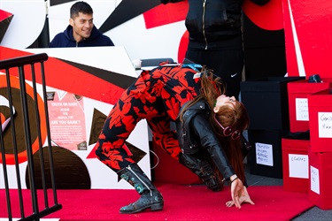 A person wearing a black and red outfit poses in a backwards bridge pose on a red stage. 