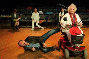 A man wearing a dark coloured jacket lies on the ground next to a woman in red wheelchair.