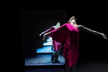 A person wearing a red sarong leans their head back and stretches their arms out to the side. Behind them is a mirrored image of their actions.