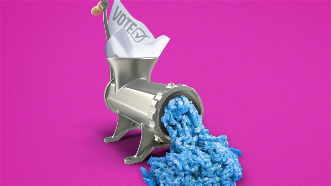 A meat grinder with a white paper sticking out of its feeder with the word 'Vote' on it. At the other end is a mess of blue foam.