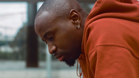 A Black man is in profile leaning forward. A gold earring is in his ear.