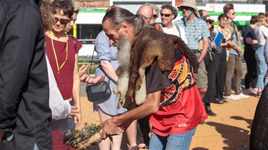 An Aboriginal Elder leads a crowd through a smoking ceremony.