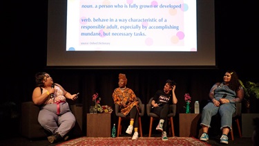 A panel of women sit under a projection screen.