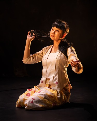 A person sitting on their heels stroking a strand of long dark hair.