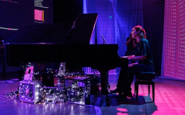 A woman with red hair sits behind a grand piano.