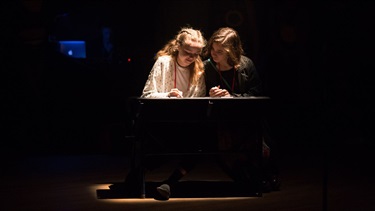 Two young girls sit at a desk under a spotlight.