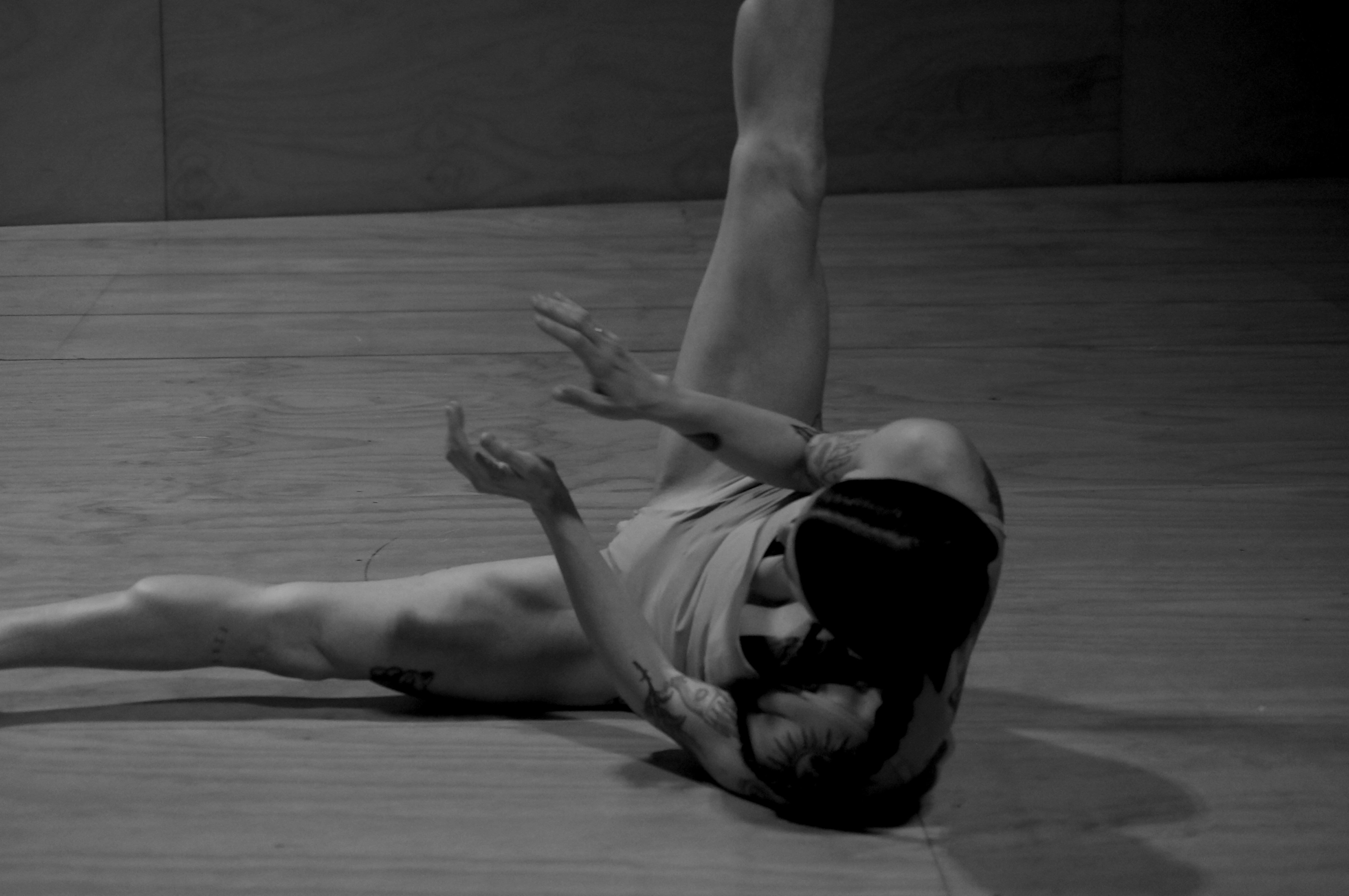 A black and while photo of a person rolling on the ground with legs stretched in the air apart.