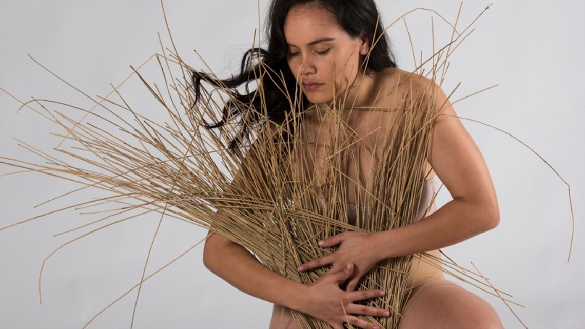 A woman with long dark hair hugs dried wheat strands in front of her chest.