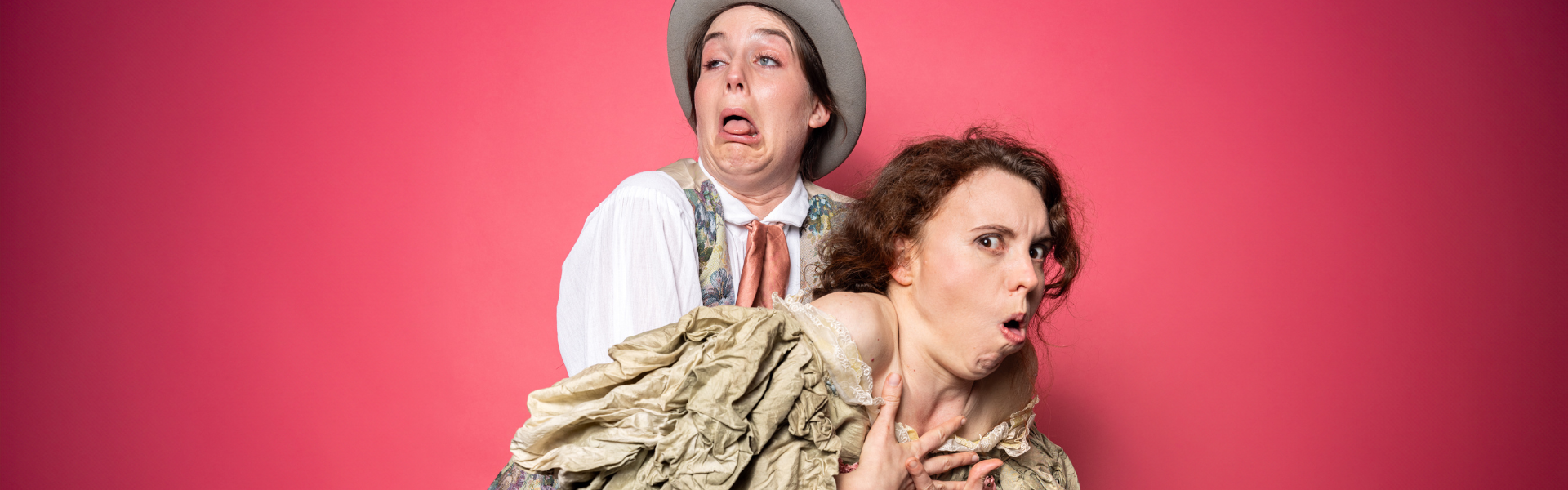 Two people hold on to one another. They wear 1940s clothing and make silly faces.