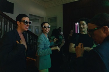 People wearing large sunglasses mingle in a room.
