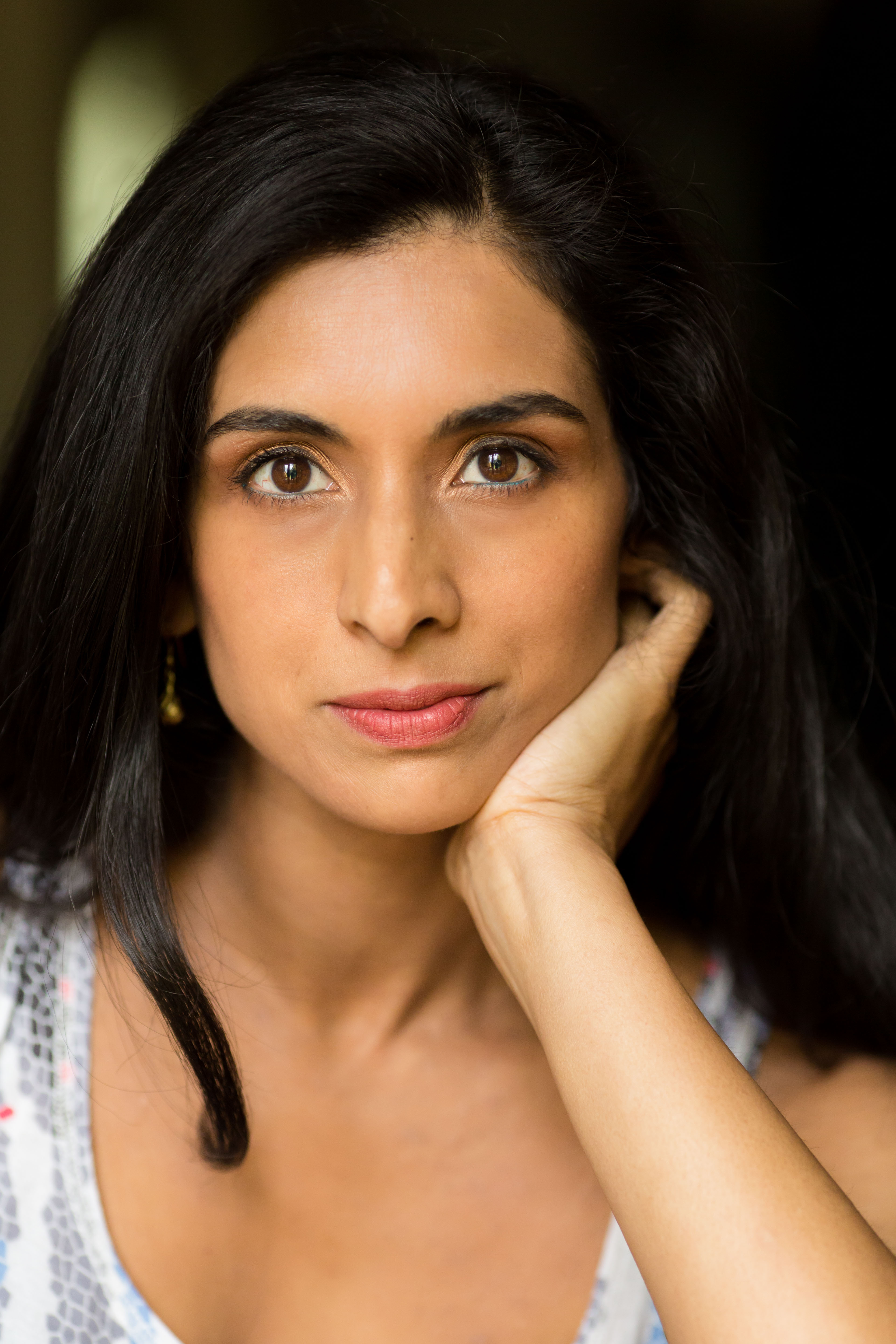 A woman with long dark hair leans her chin in the palm of her hand.