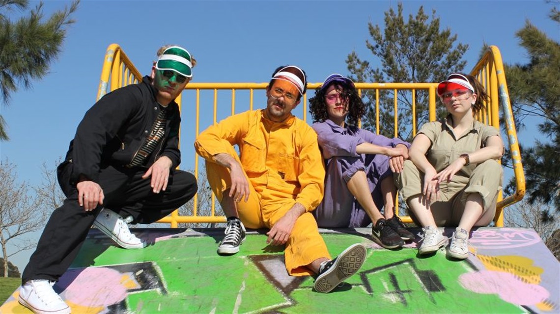 A group of people wearing 80s track suits and neon-coloured visor hats sitting on a graffiti painted skate ramp.