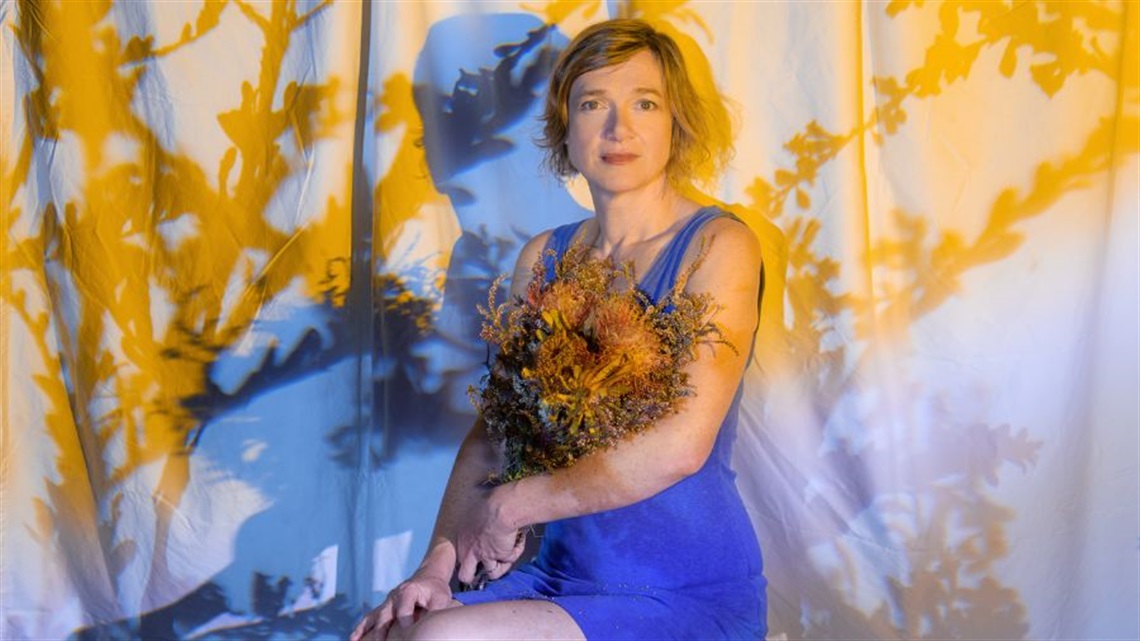 A woman in a blue dress sits on a stool.