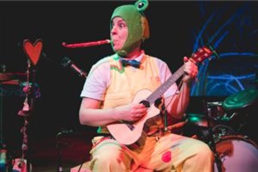A person wearing a frog hat sits to play a ukele.