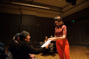 A woman passes on a document to another woman seated in the audience.