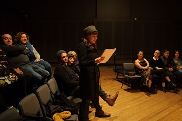 A person stands in front of an audience reading a document.