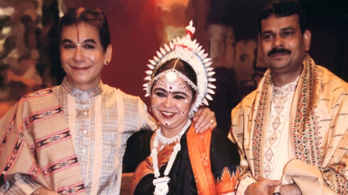 Two men and a woman cluster together wearing cultural outfits.