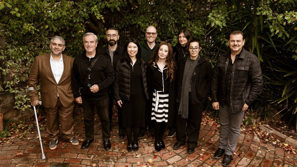 A group of people cluster together in front of trees.