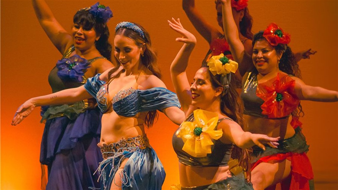 A group of South Asian woman wear multi-coloured traditional sarongs and spread their arms in various directions.