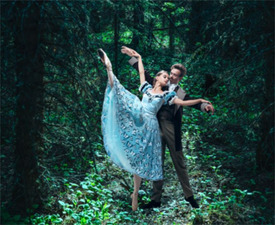 Two ballet dancers in a leafy glade. A man in a suit stands behind a woman in a dress, supporting her as she raises one leg in the air.  