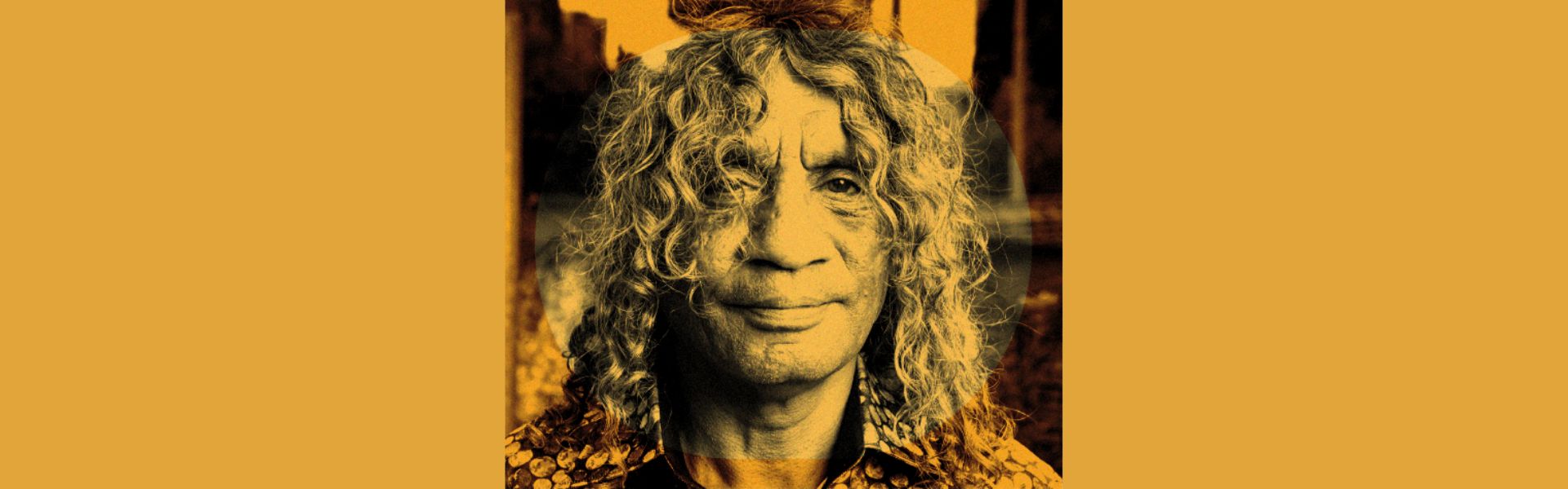 An aboriginal man with long curly hair is wearing a buttoned shirt. A yellow hue overlays the image.