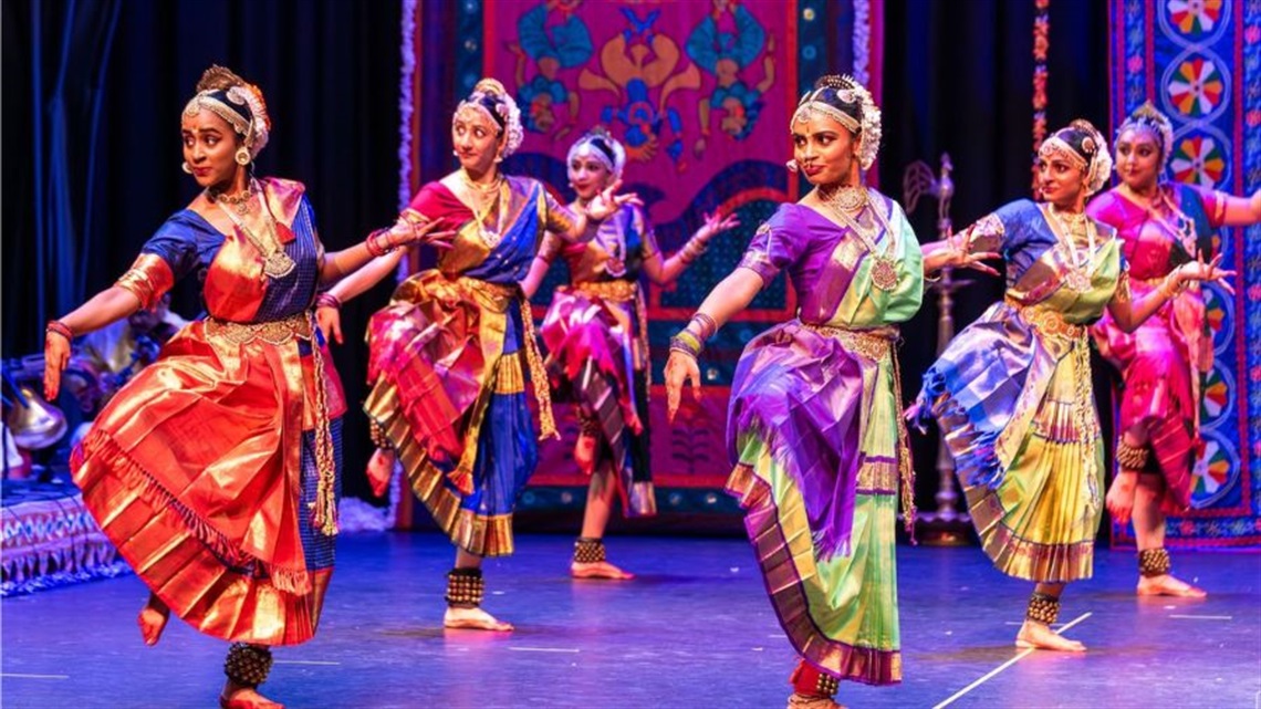 A group of female Indian dancers dressed in traditional clothing dance across a stage.