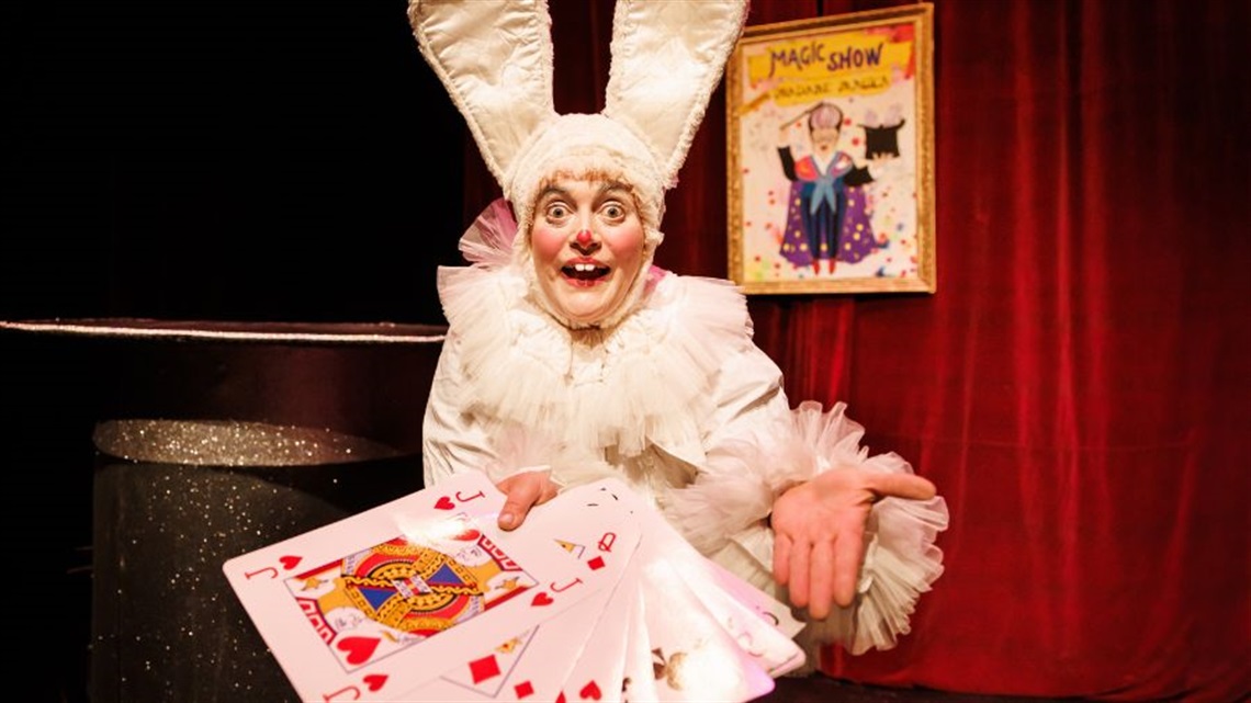 A person dressed in a rabbit costume holds out a fan of large playing cards.