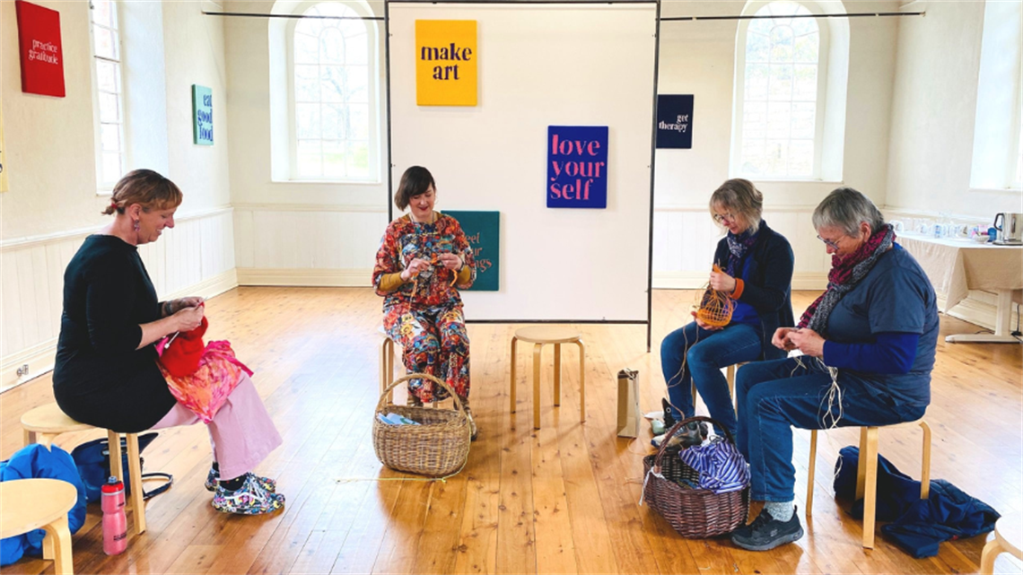 A group of people gather in a circle working on craft projects