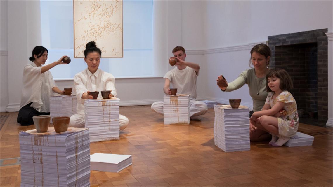 A group of people gather pouring tea over stacks of white paper